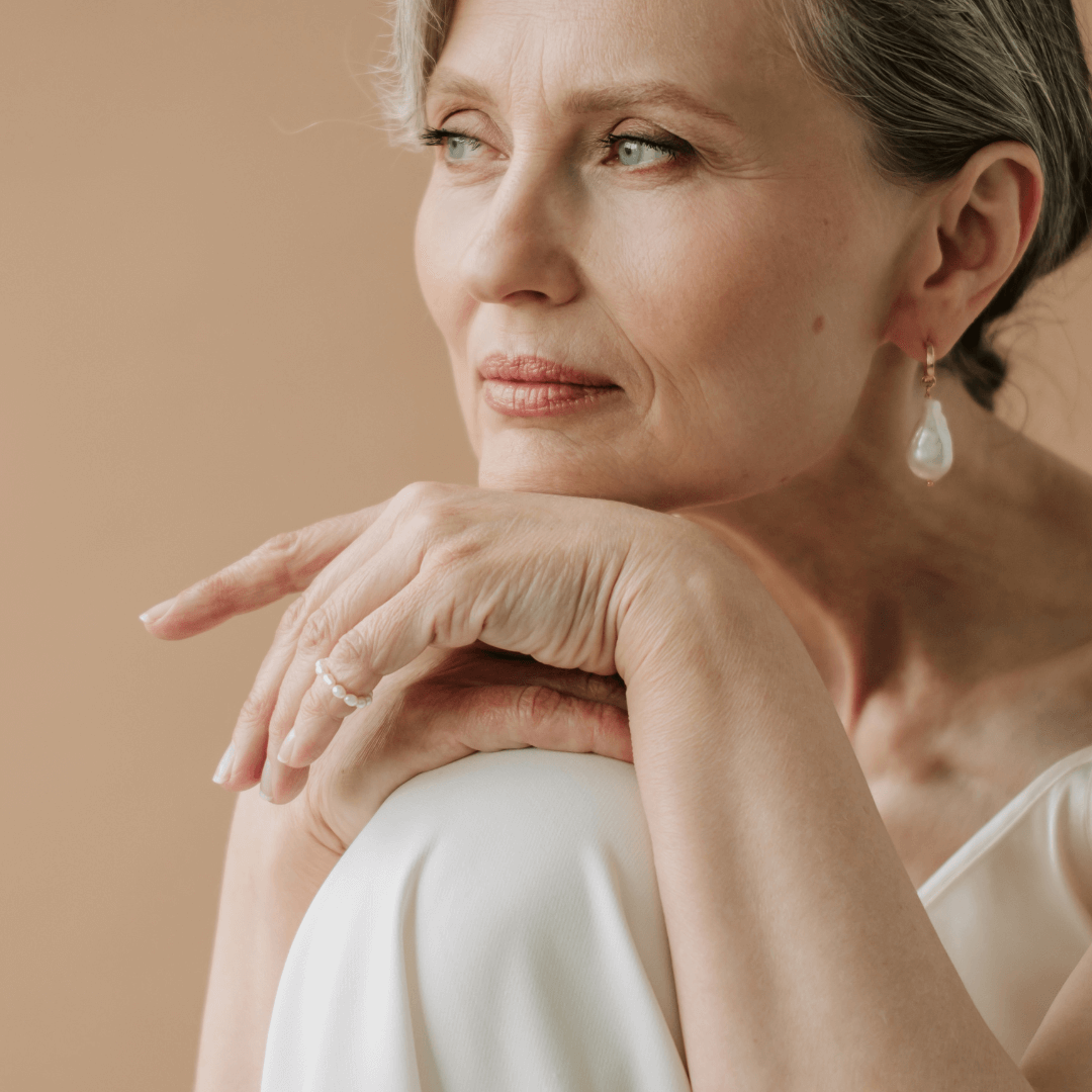 The Psychology of Jewellery: Why What You Wear Changes How You Feel. The confident woman is wearing earrings and a ring on a white outfit in a neutral background.