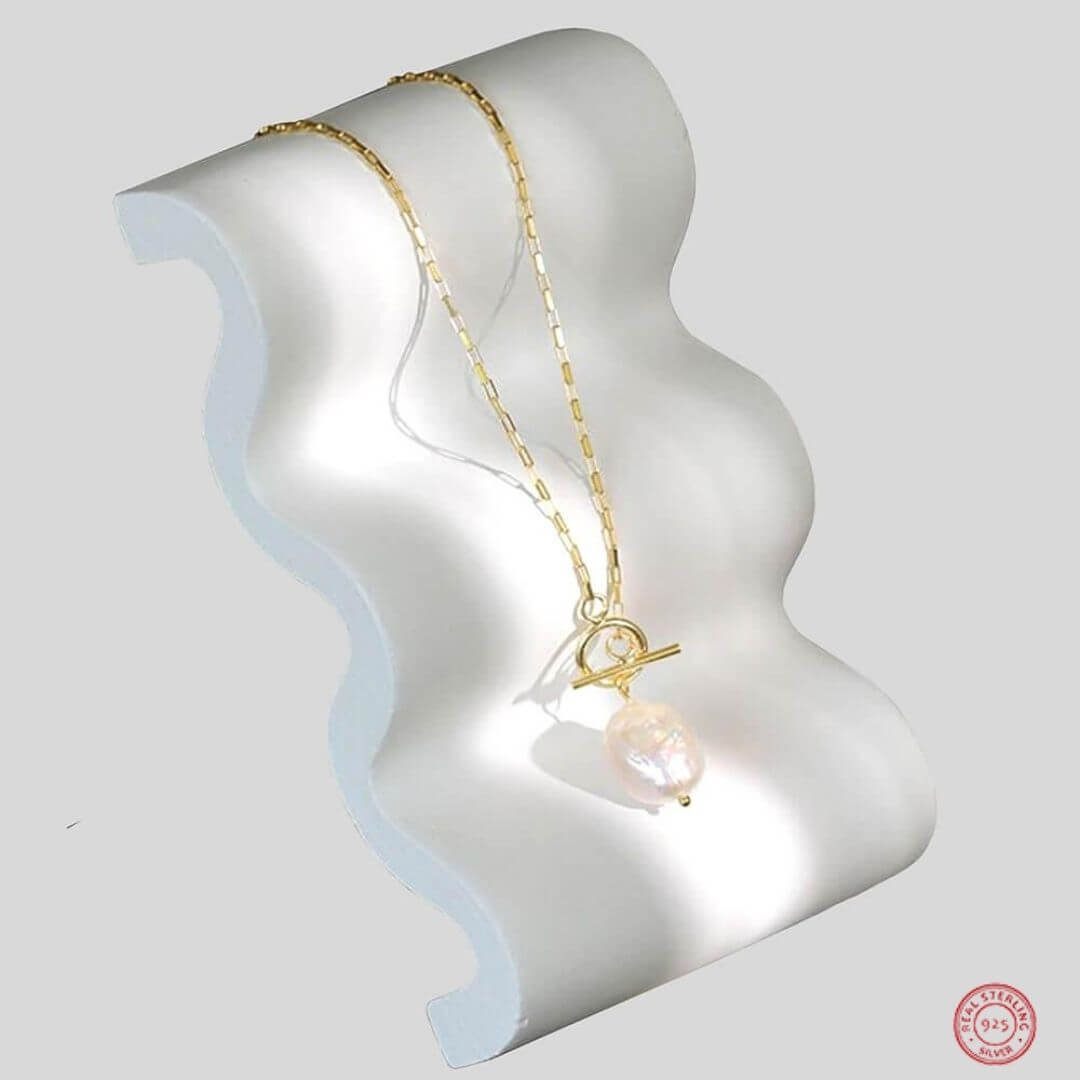 A sterling silver necklace with a gold-tone finish, featuring a baroque freshwater pearl pendant, displayed on a white stand-Belle de Soiree gold pearl necklace