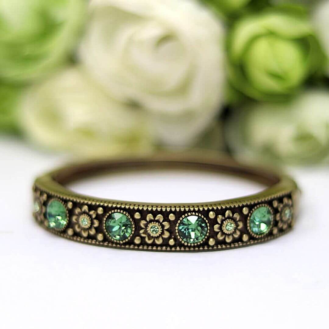 Brass bracelet with green gemstones on a white surface with blurred green flowers in the background