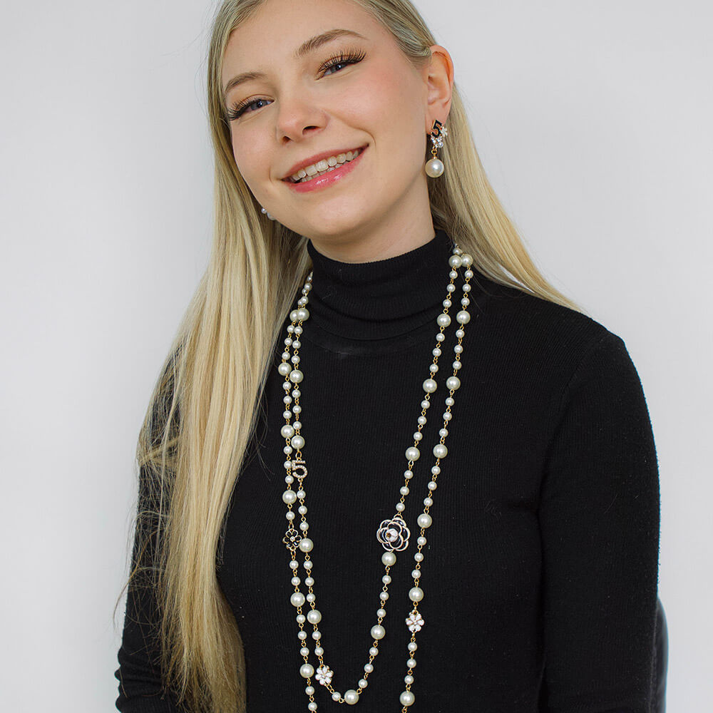 Woman wearing a long pearl necklace with matching earrings and a black turtleneck against a white background
