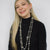 Woman wearing a long pearl necklace with matching earrings and a black turtleneck against a white background