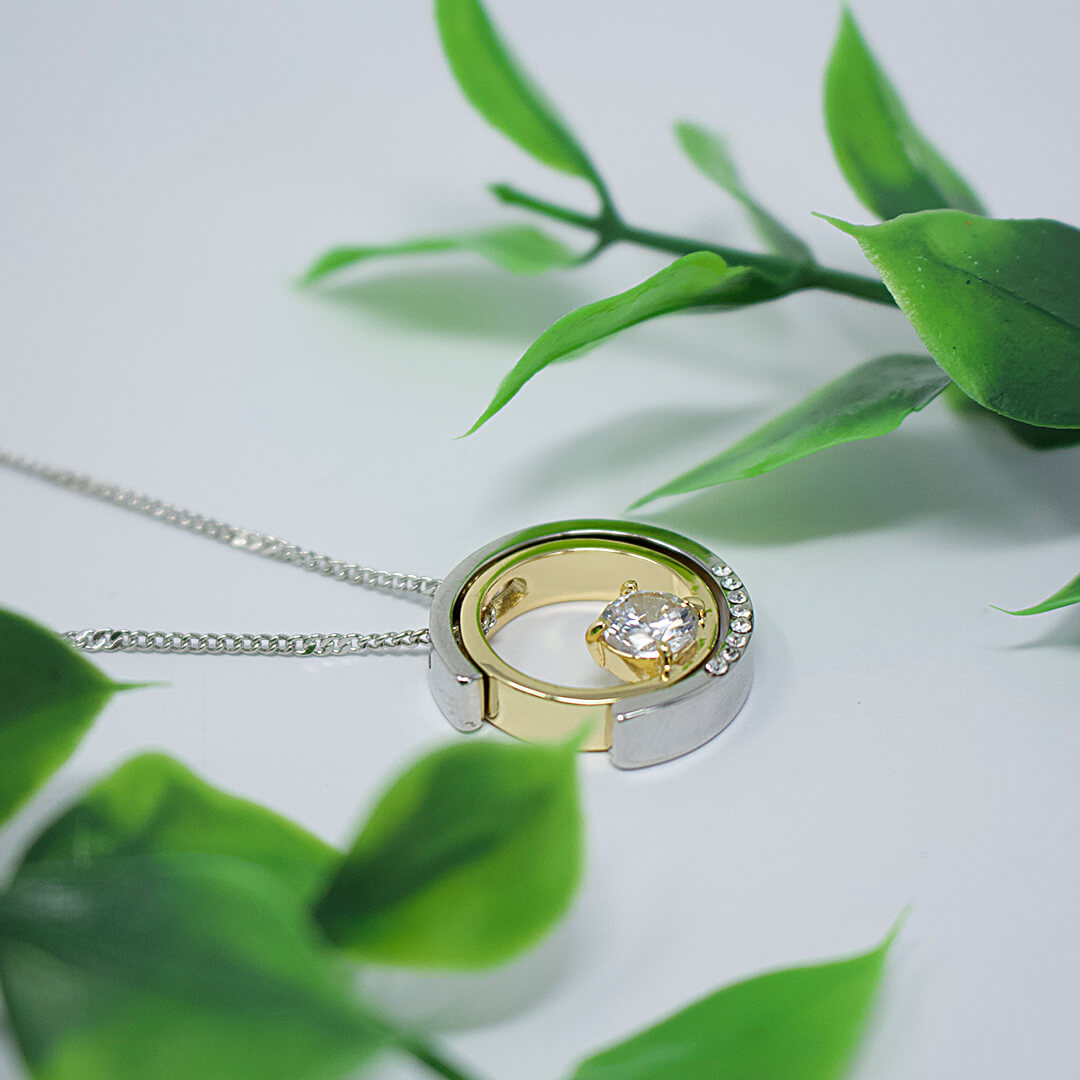 Gold and silver ring pendant with a diamond on a white background with green leaves.