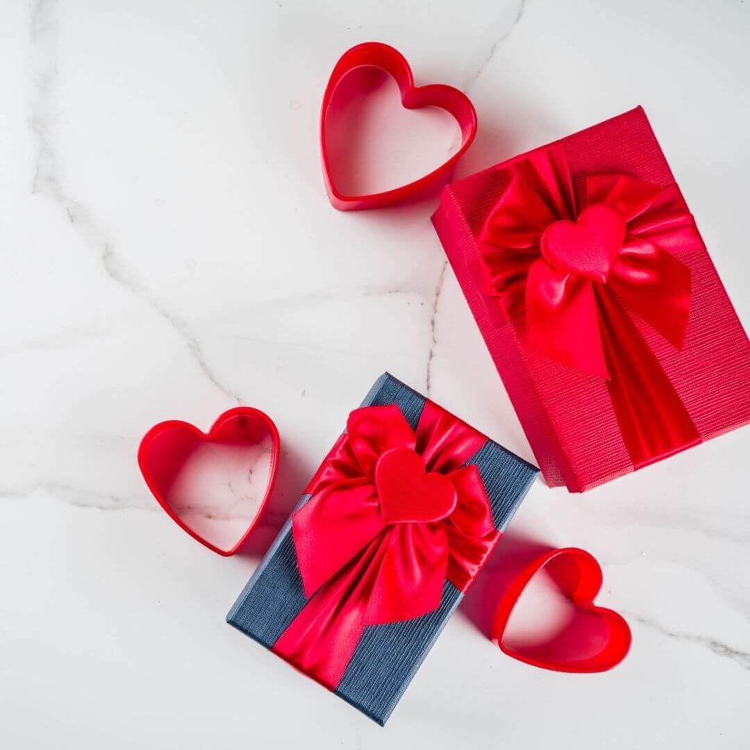 Two gift boxes with red ribbons and heart-shaped cookie cutters on a white surface-check our love gifts-Belle de Soiree