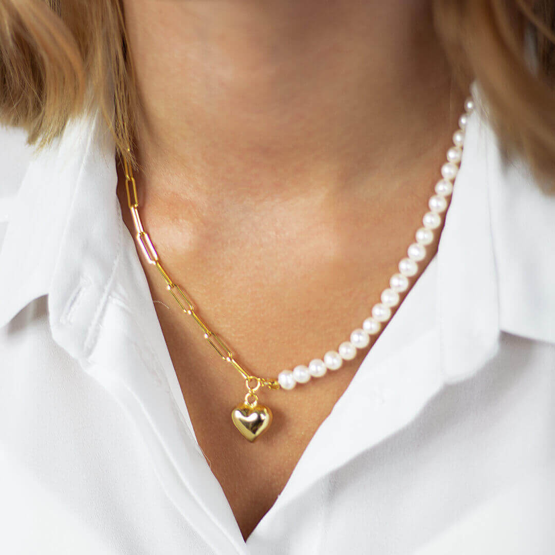 A sterling silver gold-tone necklace with an asymmetrical chain design featuring a heart-shaped pendant in the center, adorned with white pearls on one half and a gold chain on the other- BELLE DE SOIREE heart gold & pearl necklace