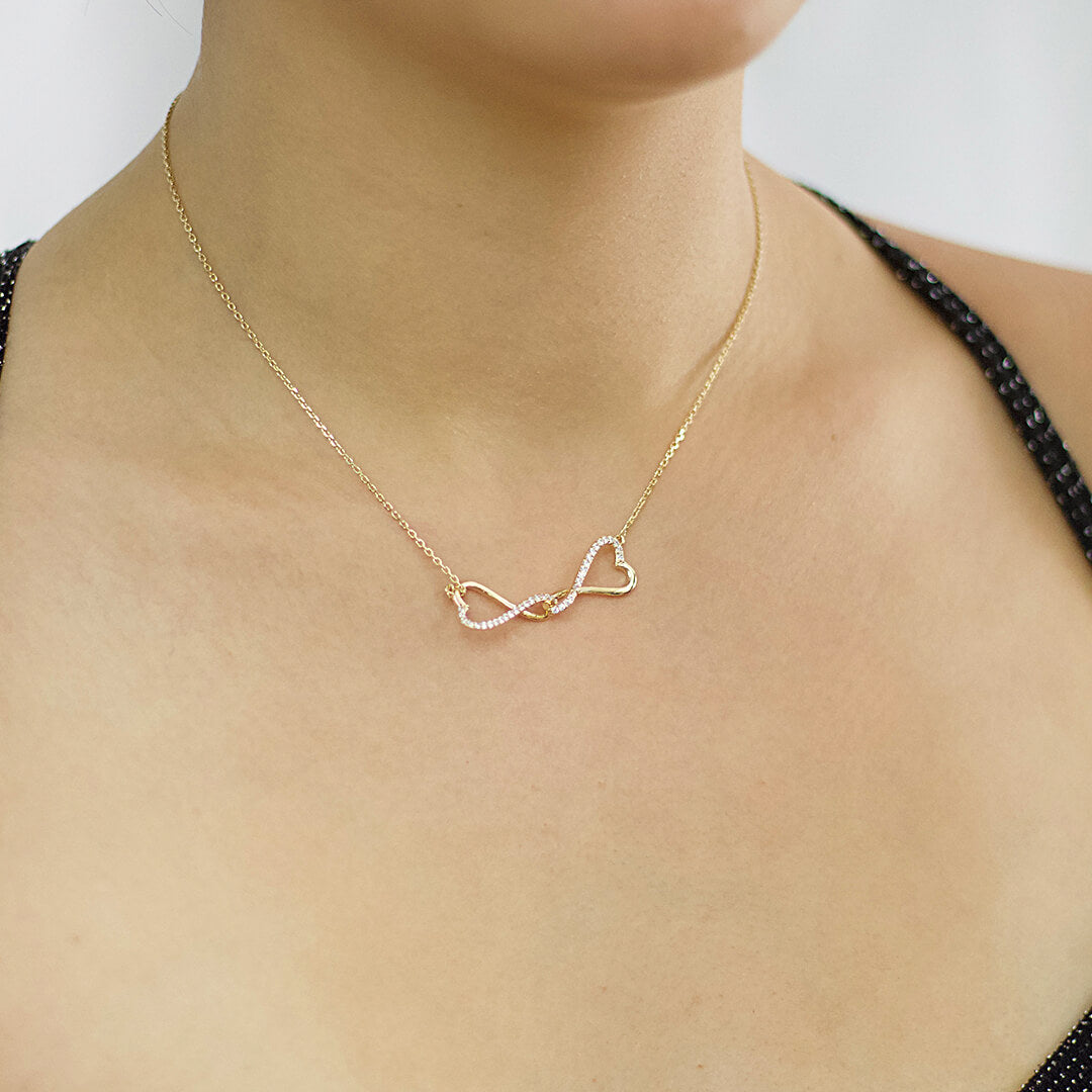 A close-up image of a woman wearing a gold-coloured two-hearts necklace made of cubic zirconia-BELLEDESOIREE
